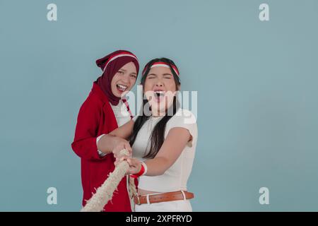 Deux joyeuses indonésiennes portant un bandeau drapeau tirent sur une corde, rejoignant la compétition pour le jour de l'indépendance indonésienne. La scène est légère Banque D'Images