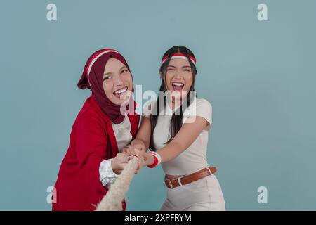 Deux joyeuses indonésiennes portant un bandeau drapeau tirent sur une corde, rejoignant la compétition pour le jour de l'indépendance indonésienne. La scène est légère Banque D'Images