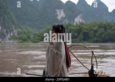 Fille Hanfu debout dans la rivière Li avec oiseau de pêche Cormoran perché sur un radeau de bambou Banque D'Images