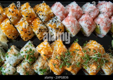 Délicieux rouleaux de sushi côte à côte dans un plateau noir. Vue de dessus sur fond noir. Banque D'Images