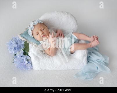 Fille nouveau-née en dentelle Robe se trouve sur la chaise dans les tons blancs et bleus photo Banque D'Images