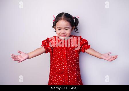 Une jeune fille asiatique en bas âge exprime un esprit pour le jour de l'indépendance indonésienne, portant une chemise rouge, debout sur un fond blanc. Banque D'Images