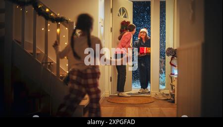 Jeune mère rencontre Grand-parent par la porte dans une maison décorée avec des guirlandes, petit garçon et fille courir pour rencontrer leur grand-mère avec des cadeaux de Noël et des cadeaux Banque D'Images