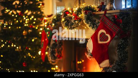 Plan vide représentant la magie des fêtes lors d'un paisible réveillon de Noël enneigé : gros plan sur une cheminée décorée avec des bas à côté d'un arbre de Noël. Guirlandes, rubans et lumières verts et rouges Banque D'Images