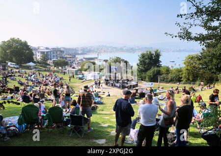 Une foule de gens se sont rassemblés dans les jardins de Prince Albert surplombant la baie de Swanage pour profiter du soleil et regarder le groupe de rock indépendant Galaxy Thief, Dorset, Angleterre, Royaume-Uni Banque D'Images