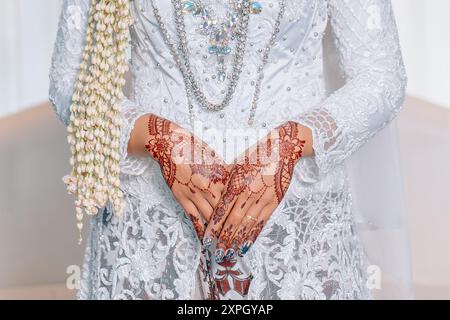 Les mains Hennaed d'Asian bride. Kebaya blanc indonésien avec décoration de fleur de jasmin Banque D'Images