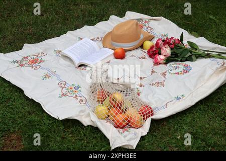 Bouquet de roses, pommes, livre ouvert et chapeau de paille sur une couverture de pique-nique. Activités du week-end d'été. Concept de vie saine. Banque D'Images