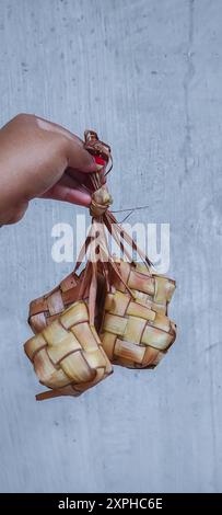 Une main de femme tenait ketupat cuit ou paquet de gâteaux de riz d'Asie du Sud-est, souvent préparé pour les festivités et plat très populaire pendant l'Eid Moubarak cel Banque D'Images