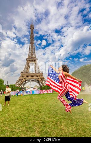 Femme américaine patriotique sautant et acclamant pour Team USA et les Jeux Olympiques de Paris 2024 devant la Tour Eiffel, Paris, France, Europe Banque D'Images