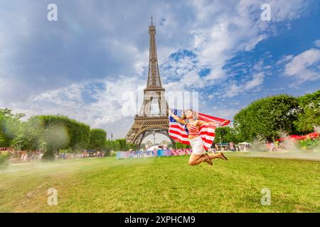 Femme américaine patriotique sautant et acclamant pour Team USA et les Jeux Olympiques de Paris 2024 devant la Tour Eiffel, Paris, France, Europe Banque D'Images