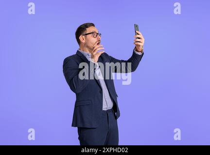 Mécontent jeune homme d'affaires choqué habillé en costume lisant des messages sur le téléphone portable. Entrepreneur professionnel masculin inquiet utilisant le téléphone portable pendant St Banque D'Images