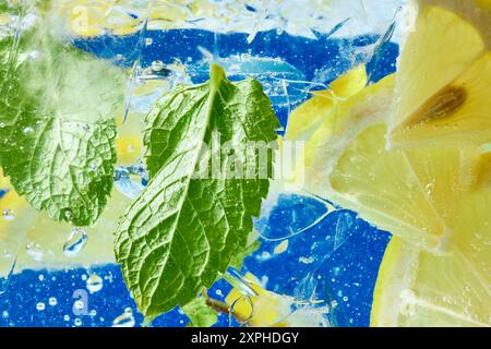 Des tranches de citron frais et des feuilles de menthe flottent dans de l'eau pétillante sur fond bleu. Papier peint texturé. Banque D'Images