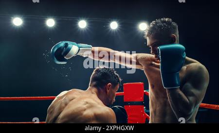 Deux boxers masculins dans un match électrisant, l'un délivrant un puissant punch sous des lumières brillantes. L'intensité et l'énergie brute du combat sont capturées, la sueur s'envole de leur corps. Championnat de boxe Banque D'Images
