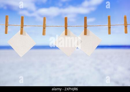 Pinces à linge en bois sur une ficelle avec des cartes blanches vierges pour le texte. Affichage des produits de montage. Concept d'été et espace de copie de fond de mer et de plage de sable Banque D'Images