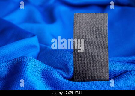 Étiquette blanche noire de vêtements de soin du linge sur fond bleu de chemise de sport en jersey polyester Banque D'Images