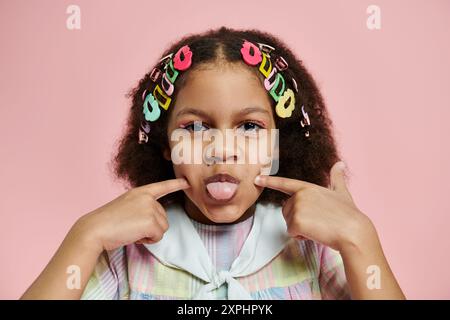 Fille afro-américaine avec des pinces à cheveux colorées sourit dans une robe rose. Banque D'Images