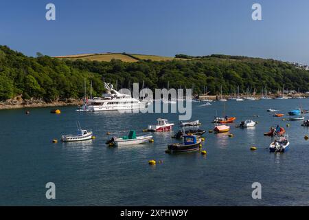 Un superbe Yacht Motor Cruiser se trouve en face de Fowey en Cornouailles. Beaucoup de petits bateaux entourent le navire avec le soleil de fin d'après-midi. Banque D'Images