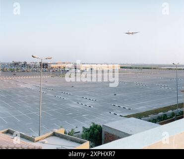 Plan large d'un vaste parking vide devant un centre commercial à Alexandrie, en Égypte, capturé en 2006. Un avion est vu voler au-dessus de la tête dans le ciel dégagé. Parfait pour les concepts de vide, d'espace et de paysages urbains. Banque D'Images