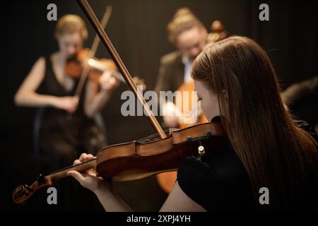 Vue arrière d'une musicienne d'orchestre méconnaissable jouant du violon avec quatuor à cordes en vedette sur scène avec des rideaux noirs Banque D'Images