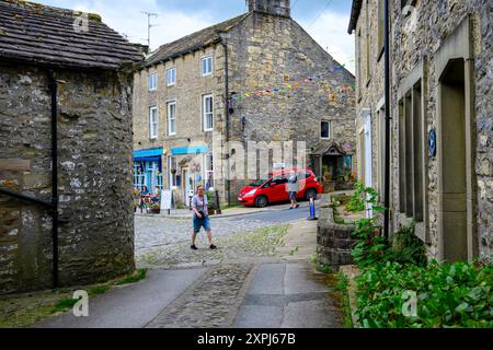 Grassington Yorkshire UK- 27 juillet 2024. Une rue pavée pittoresque dans un village pittoresque avec des bâtiments en pierre, une voiture colorée et des drapeaux. Banque D'Images