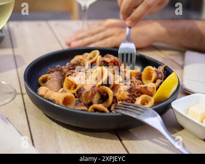 Une main avec une fourchette prête à manger des calamars frits sur une terrasse Banque D'Images