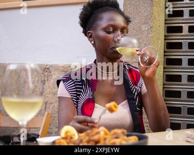 Jeune femme buvant du vin blanc tout en mangeant une tapa de calmes frits Banque D'Images