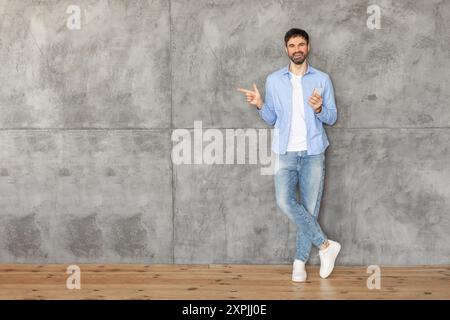 Homme appuyé contre le mur de béton gris tenant le smartphone et pointant Banque D'Images