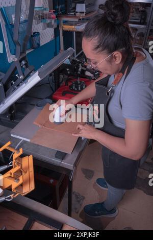 Jeune femme active dans son atelier fait le processus de sublimation avec une plaque d'étiquette, impression et concept de design graphique. Banque D'Images