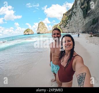 Un homme et une femme posent pour une photo sur une plage. La femme porte un débardeur rouge et l'homme porte un maillot de bain bleu. La scène est heureuse et Banque D'Images