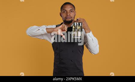 Le personnel du restaurant donne une pancarte pouces vers le bas sur fond jaune, portant un ensemble de cruet avec des condiments essentiels aux tables. Serveur dans l'industrie du service à la clientèle, n'aime pas le symbole. Caméra B. Banque D'Images