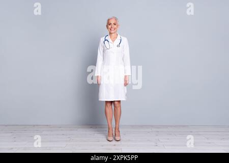 Photo pleine longueur de charmante dame senior médecin spécialiste qualifié cardiologue porter une robe blanche isolée sur fond de couleur grise Banque D'Images