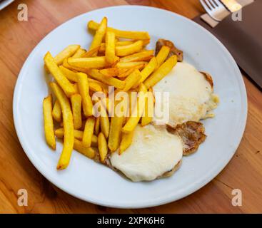 Steaks de porc nappés de mozzarella fondue servis avec des frites Banque D'Images