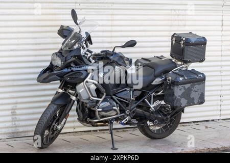 La moto noire avec un logo BMW à l'avant est garée sur le bord de la route. La moto a un coffre à bagages attaché à l'arrière et un sui Banque D'Images