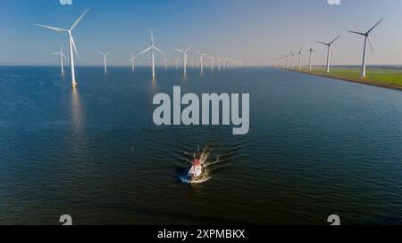 Une soirée tranquille se déroule alors qu'un petit bateau de pêche glisse dans des eaux calmes, encadrées par d'imposants moulins à vent s'étendant à travers l'horizon. Bateau de pêche avec moulins à vent à Ijsselmeer pays-Bas Banque D'Images