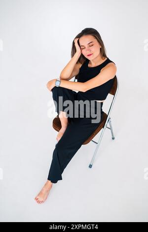 brunette en pantalon noir est assise sur une chaise et tient sa tête Banque D'Images