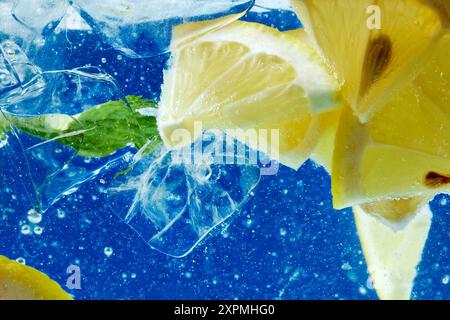 Tranches de citron et feuilles de menthe immergées dans de l'eau pétillante. Essence de boisson estivale rafraîchissante et savoureuse avec fond bleu. Papier peint texturé. Banque D'Images