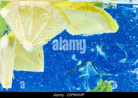 Tranches de citron juteuses et feuilles de menthe dans de l'eau pétillante. Ambiance estivale vibrante et rafraîchissante sur fond bleu vif. Papier peint texturé. Banque D'Images