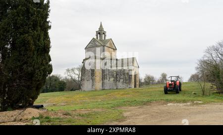 Arles, France - 8 mars 2023 : Chapelle de la Sainte Croix sur un matin nuageux en hiver, tracteur rouge Banque D'Images