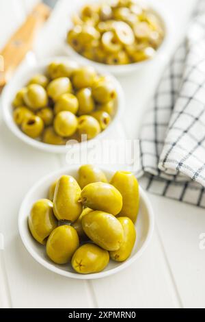 Olives vertes marinées en saumure dans un bol sur une table blanche. Banque D'Images