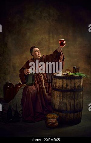 Homme, moine médiéval soulevant un verre de bière, pinte de bière sur fond vintage sombre. Riche héritage des traditions brassicoles de l'abbaye Banque D'Images