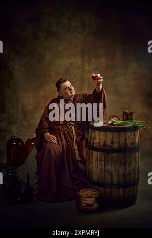 Homme, moine médiéval soulevant un verre de bière, pinte de bière sur fond vintage sombre. Riche héritage des traditions brassicoles de l'abbaye Banque D'Images