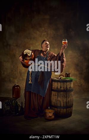 Moine médiéval, homme en vêtements d'époque avec baril de bière et pinte levant verre de bière sur fond vintage. Ancien artisanat de ALE monastique Banque D'Images