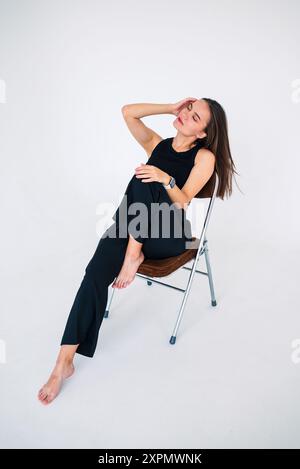 une fille en vêtements noirs est assise sur une chaise et redresse ses cheveux avec sa droite Banque D'Images