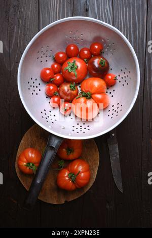 Vue de dessus sur les tomates rouges mûres dans passoire en métal rustique et couteau sur la table en bois. Photographie culinaire Banque D'Images