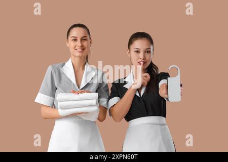 Jeunes femmes de chambre avec des serviettes propres et un cintre de porte sur fond brun Banque D'Images