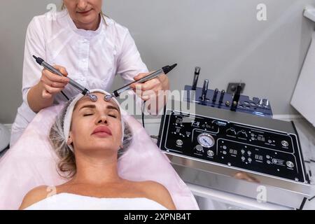 Vue de dessus de la femme et cosmétologue fait la procédure professionnelle de microcourant. Cosmétologie matérielle et soins de la peau. Banque D'Images