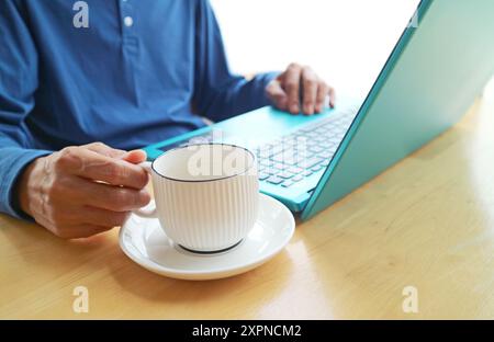 Gros plan de la main tenant une tasse de café tout en travaillant sur ordinateur portable Banque D'Images
