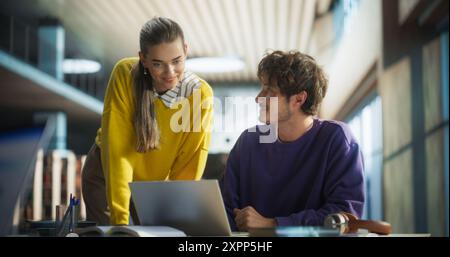 Étudiants femmes et hommes étudiant dans une bibliothèque collégiale. Femme aidant son camarade de classe à faire ses devoirs sur un ordinateur portable. Couple utilisant un ordinateur portable pour un projet de recherche de groupe Banque D'Images