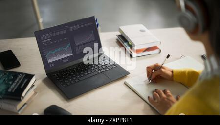 Prise de vue au-dessus de l'épaule avec un étudiant étudiant en commerce et finance dans une bibliothèque. Anonymous Female Learning Online, se préparer pour les examens de gestion Banque D'Images