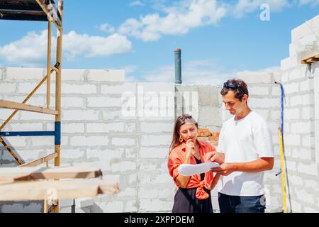 Homme ingénieur architecte montrant la maison en construction à la femme future propriétaire vérifiant le plan directeur. Consultation pendant le projet tout en construisant wi Banque D'Images